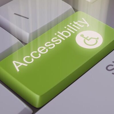 An image of a green computer keyboard key labeled "Accessibility" with an icon of a person in a wheelchair. White light radiates up from the text and image on the surface of the keyboard.